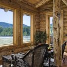 Photo of custom log home sitting room with wicker chairs and view through large pine trimmed windows of river and forest.