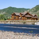 Photo of luxury log home viewed from across Yampa river with mountains in background.