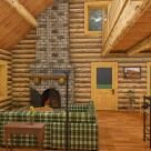 Rendering of log home living room with stone fireplace, green couch and breakfast bar.