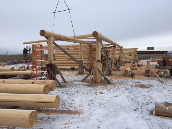 A tower crane moves the next log into place to be scribed and fitted in the shell of this handcrafted log home.