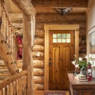 Interior of log home entry door with red runner carpet and log rails on log staircase
