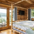 Log home bedroom with log bedframe and view to firepit and lake