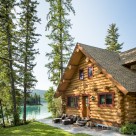 A handcrafted log home with full log gable end and red window trim with trees and lake in background