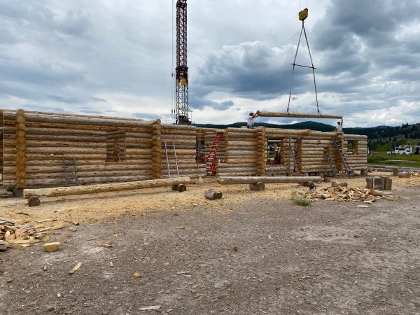 A tower crane with tongs and a spreader bar assembly make guiding the full length logs much easier and safer when building custom log homes.